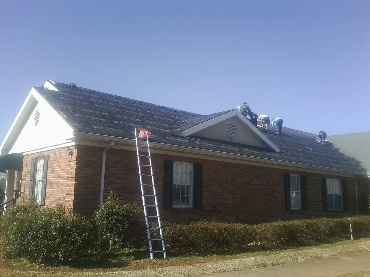 Crew tearing shingles off a brick ranch roof with a ladder set — Emergency Roof Repair work by our crew in Letart
