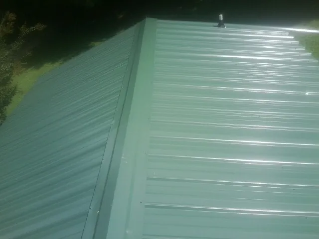 New green metal panels meeting at the ridge of a roof — Flat Roof Repair work by our crew in Letart