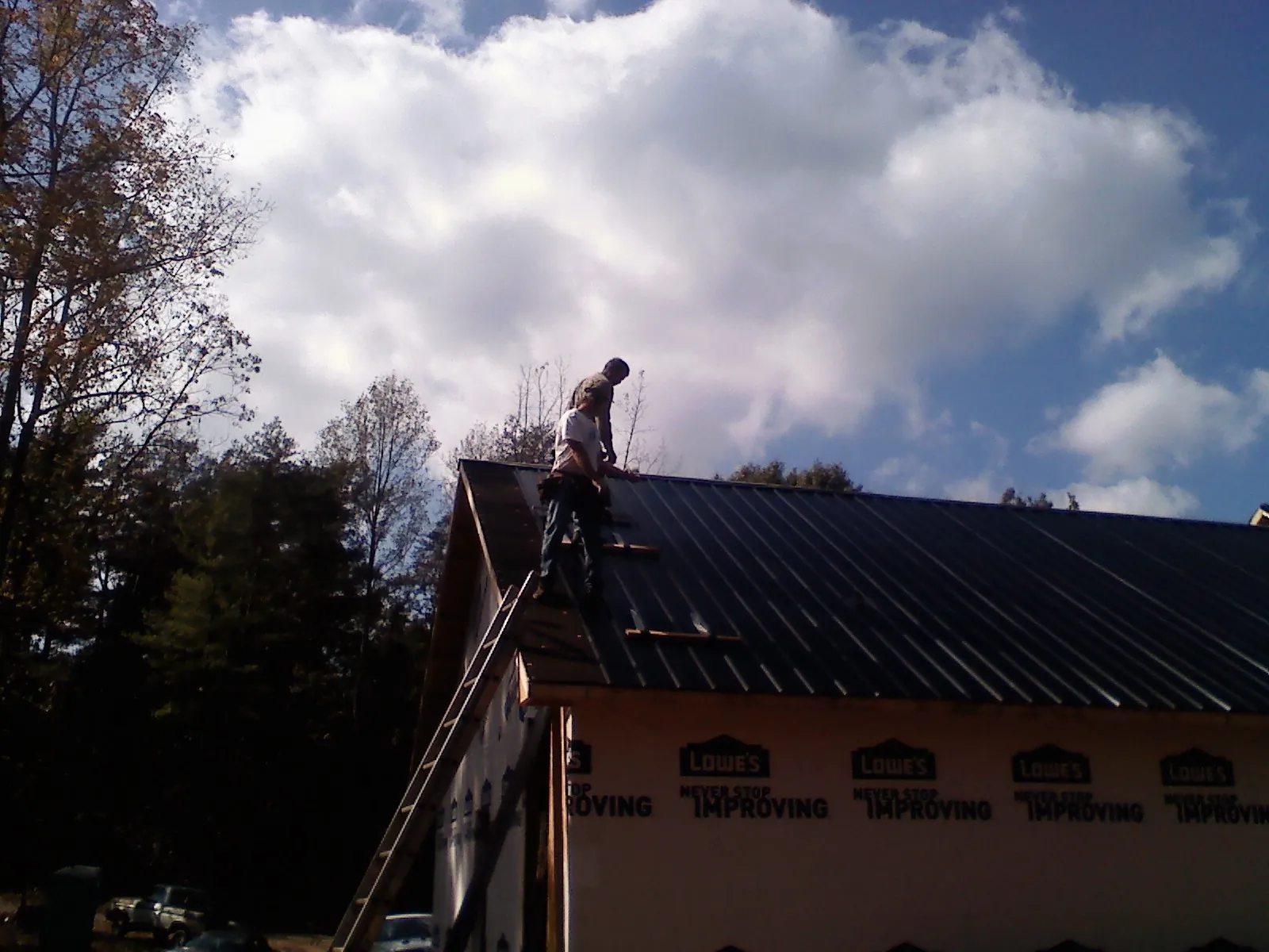 Roofer fastening dark metal panels high against a cloudy sky, from a Roof Inspection job in Letart