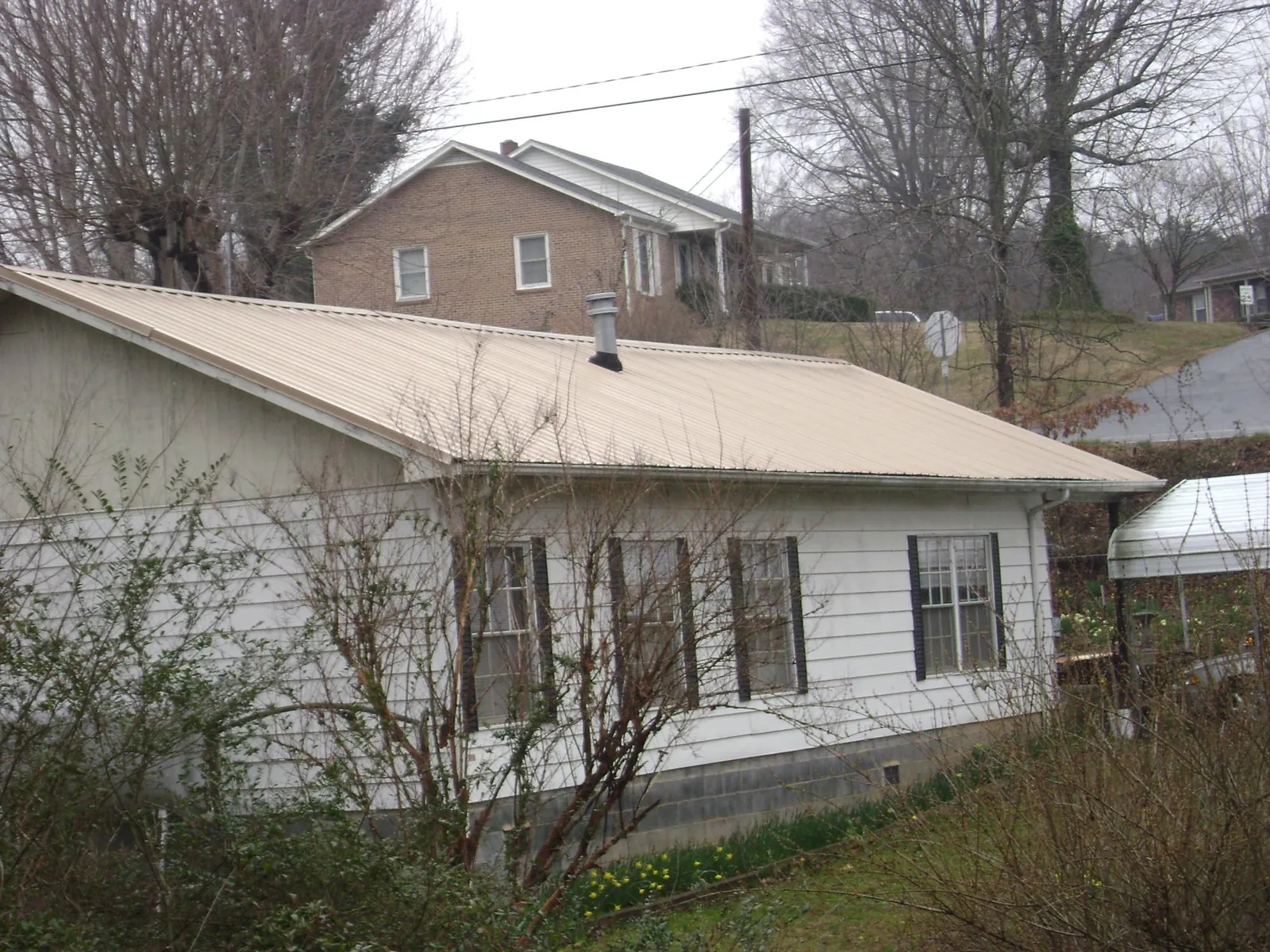 Tan metal roof on a white sided house set into a hillside — Commercial Roofing by Roofing Brothers in Letart